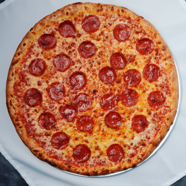 A whole, round Beach Pizza pepperoni pizza with melted cheese on a metal pan.