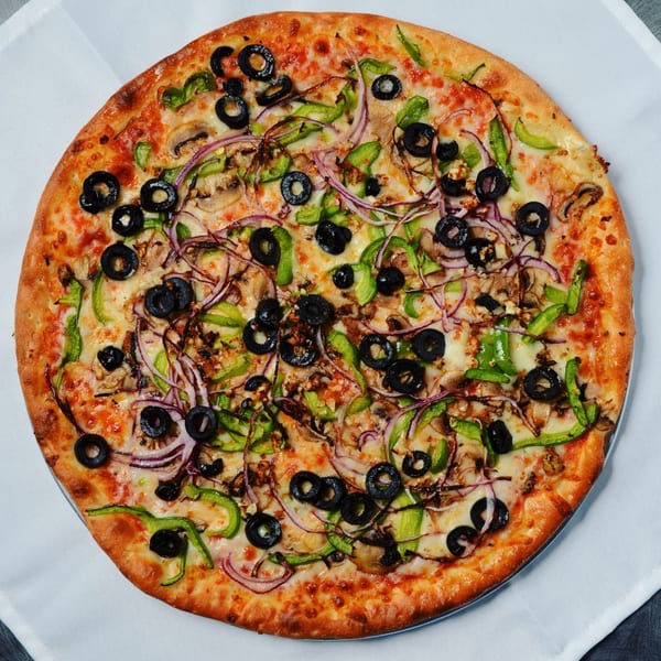 A whole Beach Pizza with black olives, green peppers, red onions, and mushrooms on a white tablecloth.