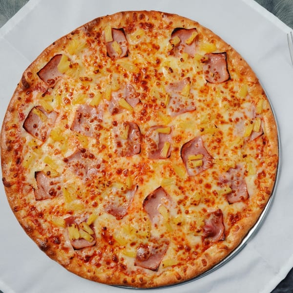 A whole Beach Pizza Hawaiian pizza, topped with ham and pineapple, on a white tablecloth.