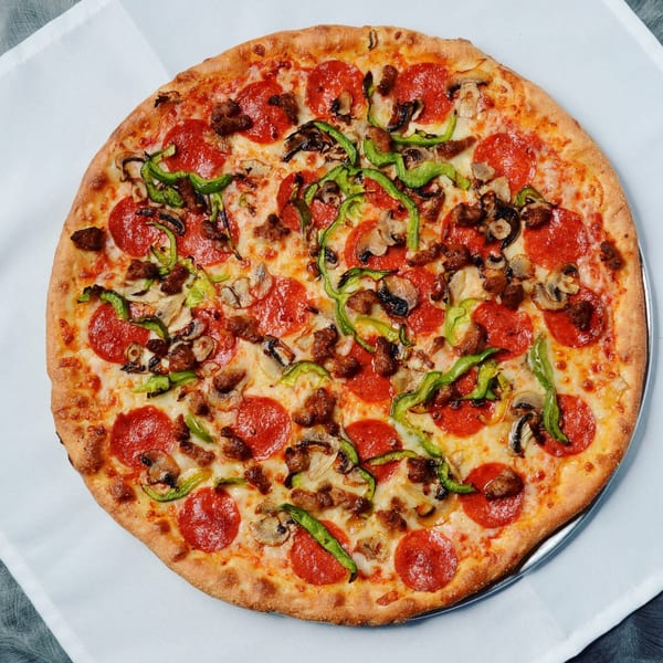 A Beach Pizza with pepperoni, green peppers, mushrooms, and sausage on a white tablecloth.